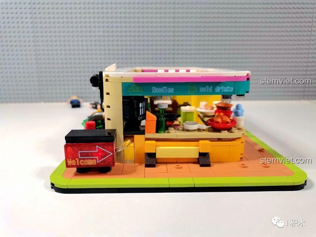 Mặt bên của mô hình Nhà hàng Trung Hoa Cyberpunk BrickCool KS003 với biển hiệu 'Welcome' có đèn, bộ lắp ghép kiến trúc cyberpunk, tạo điểm nhấn ấn tượng.