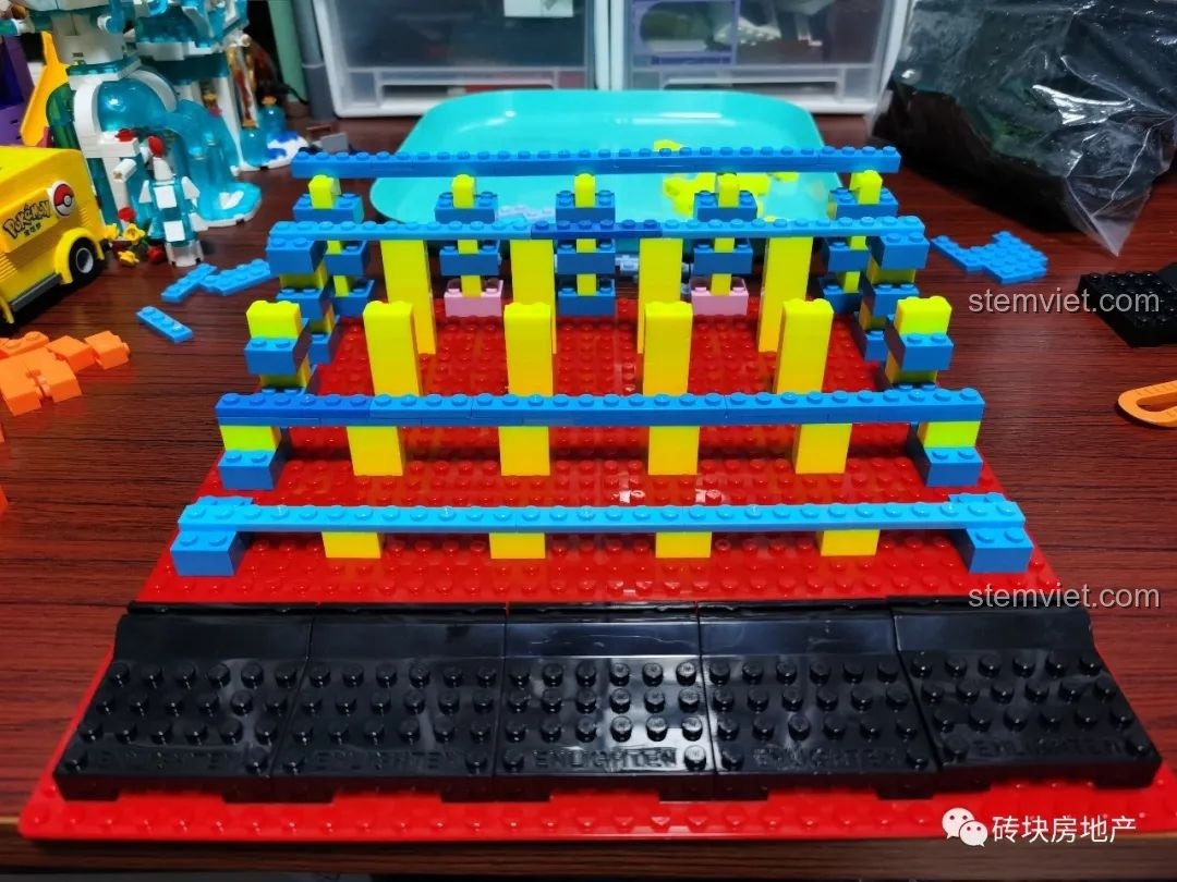 Cấu trúc bậc thang từ các mảnh ghép màu xanh, vàng, đen trên đế lắp ráp, đang trong quá trình hoàn thiện.