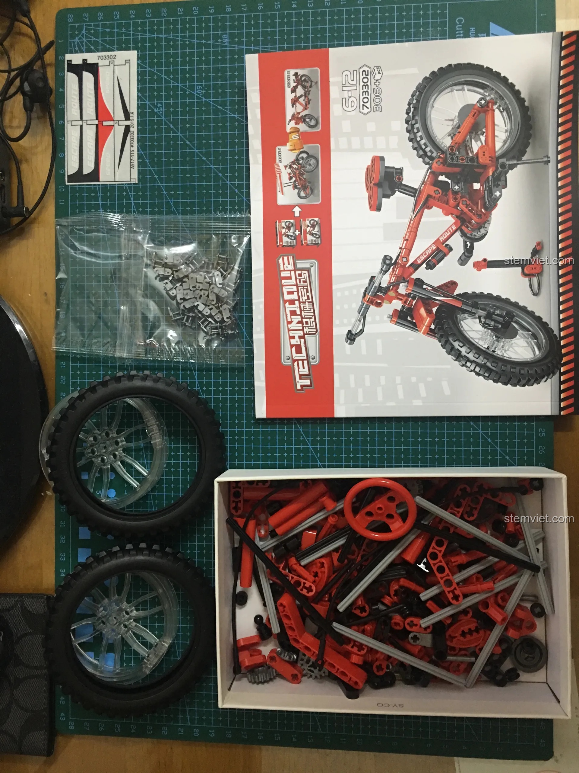 Các chi tiết của bộ Sembo 703302 được đổ ra khay, bao gồm bánh xe, mắt xích và các mảnh ghép Technic màu đỏ, đen.