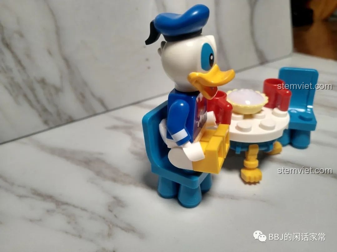 Vịt Donald đang cố gắng ngồi vào chiếc ghế nhỏ, cho thấy phần đuôi vịt bị cấn vào lưng ghế.