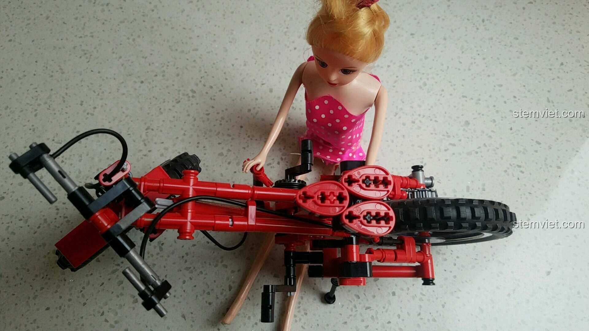 Một cô búp bê đang tạo dáng bên cạnh chiếc xe đạp địa hình Sembo 703302 đã lắp xong.
