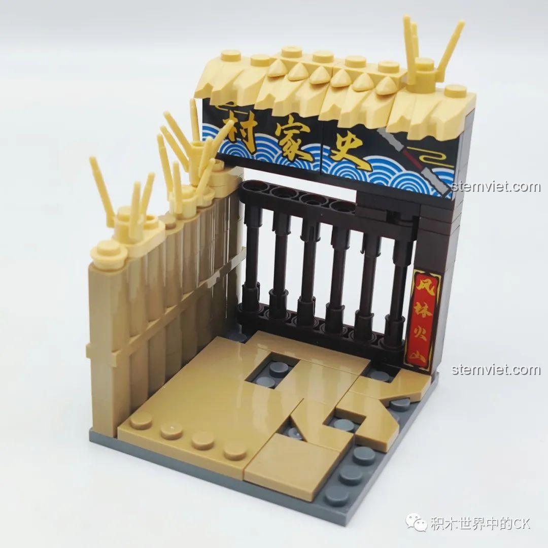 Đế trưng bày của bộ lắp ráp Decool 10802 Sử Tiến, tái hiện cổng làng Sử Gia Thôn với hàng rào tre và biển hiệu.
