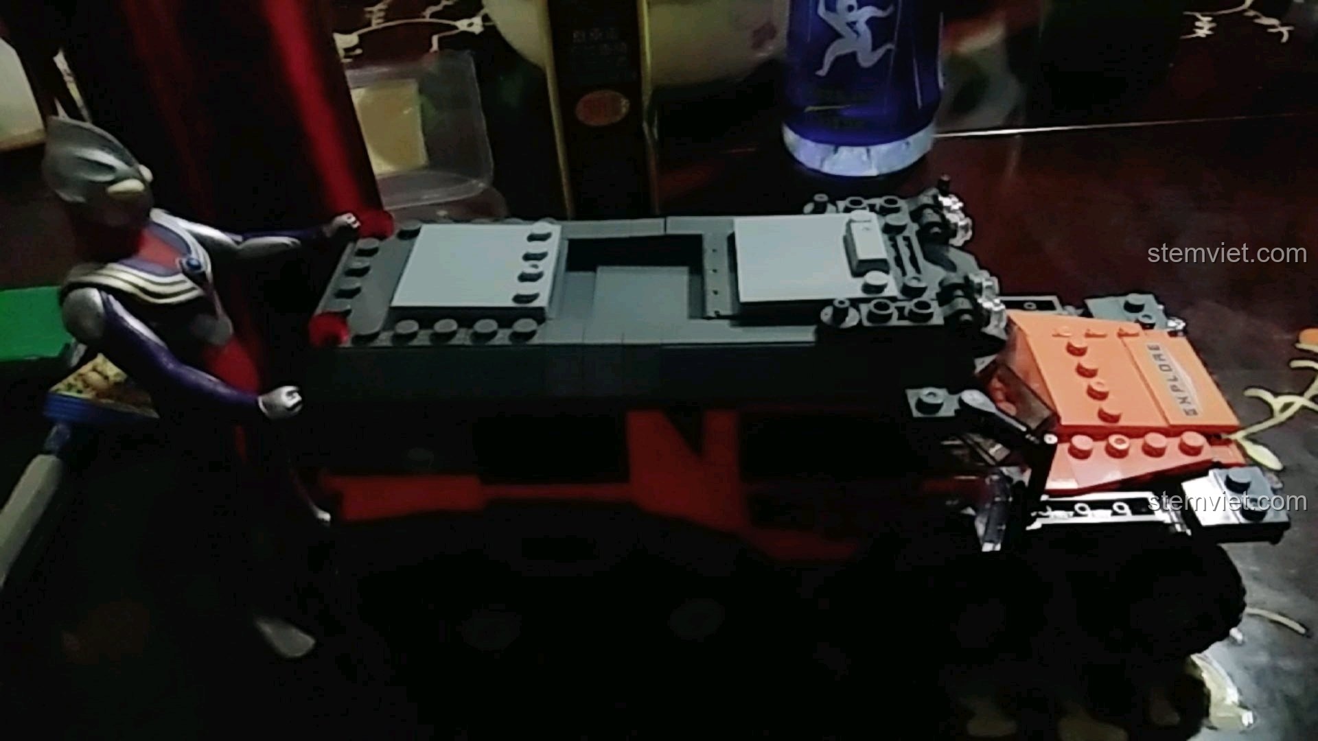 Hình ảnh vui nhộn mô hình siêu nhân Ultraman đang đẩy chiếc xe địa hình 8 bánh Xingbao trong bóng tối.