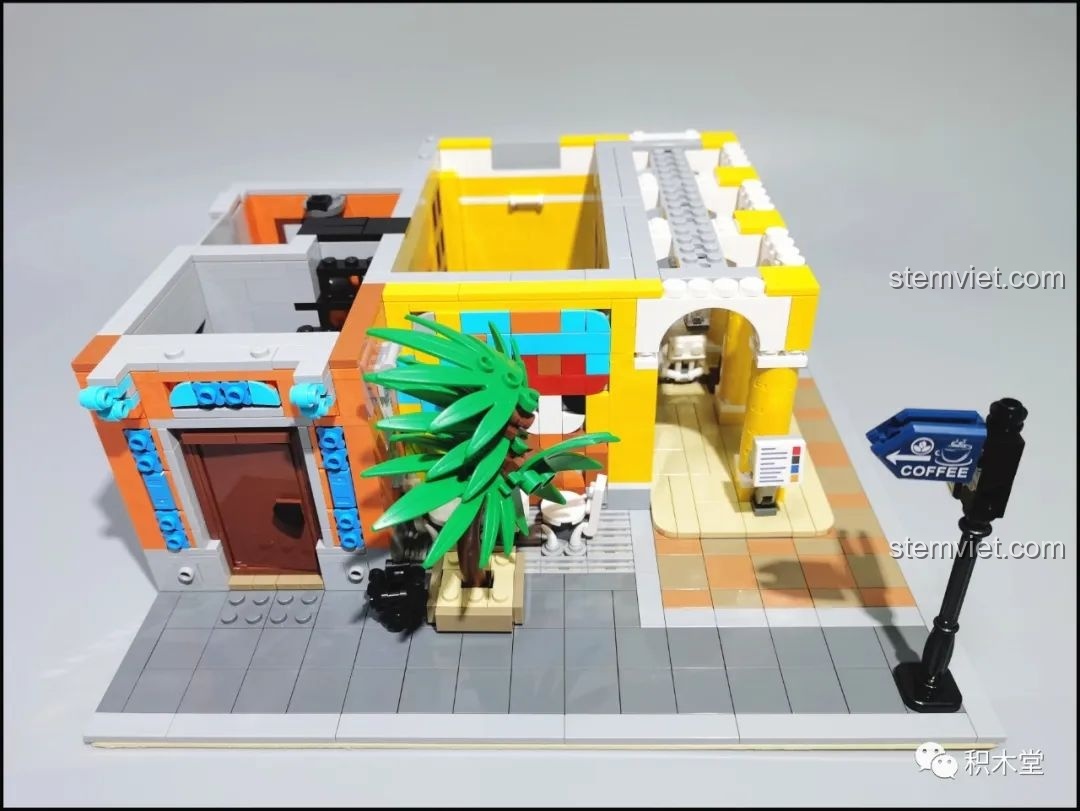 Tầng 1 của bộ lắp ráp RAEL 10002 hoàn thiện với cây cọ, bàn ghế ngoài trời và biển chỉ dẫn.