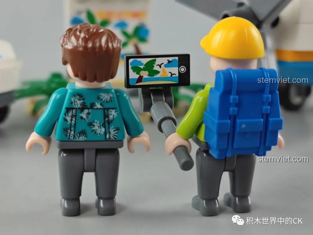 Mặt sau của hai nhân vật minifigure trong bộ GUDI 10501, một người cầm gậy selfie với màn hình hiển thị cảnh biển.