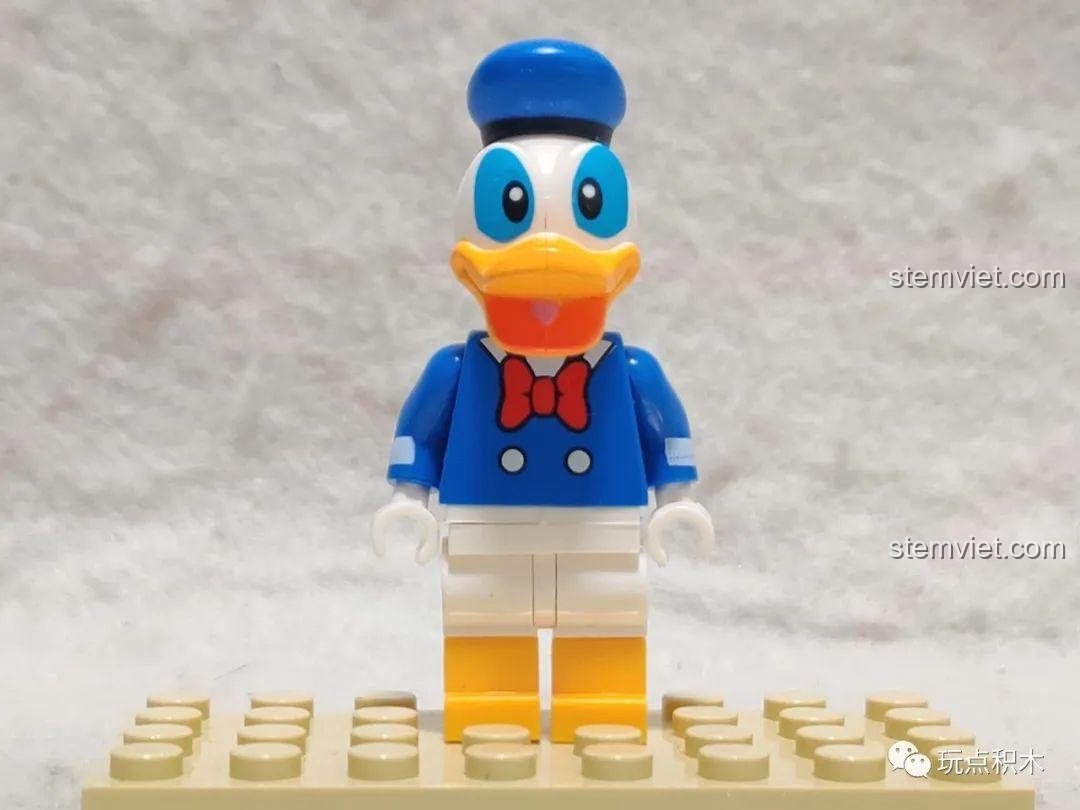 Minifigure Vịt Donald trong bộ đồ thủy thủ màu xanh, nơ đỏ, đứng trên đế trưng bày.