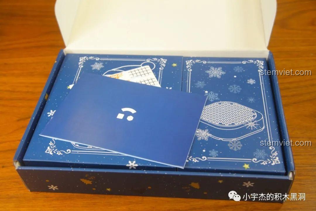 Bên trong hộp lắp ráp Hộp Nhạc Giáng Sinh Người Tuyết với sách hướng dẫn và các chi tiết được đóng gói.