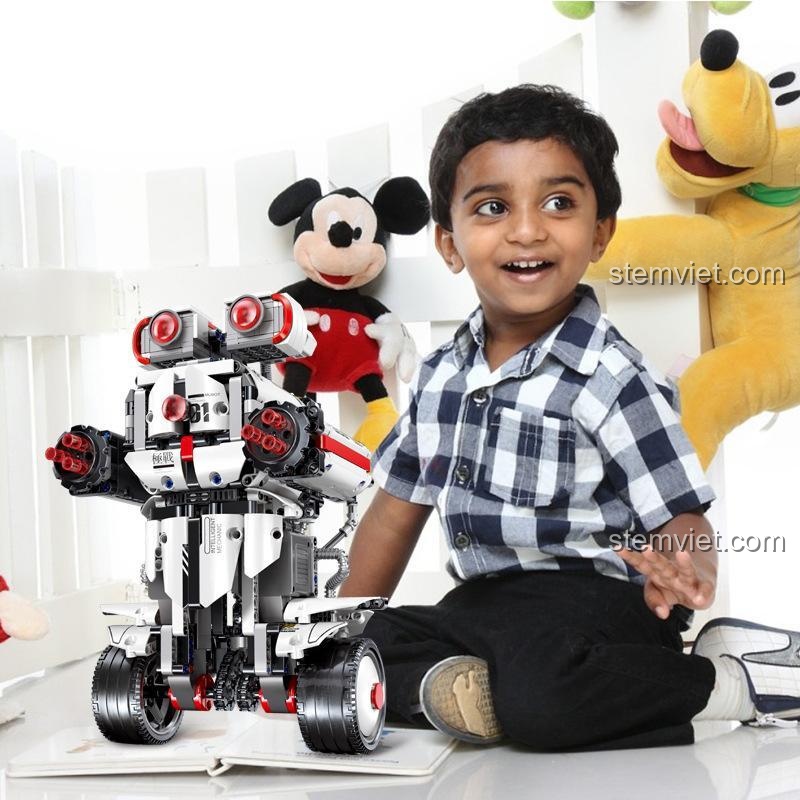 Bé trai vui vẻ bên cạnh robot giáo dục Robot Technic Tự Cân Bằng Mould King, xung quanh là các món đồ chơi khác.