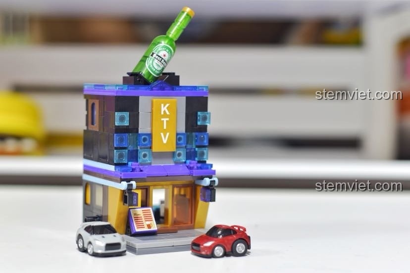 Mô hình quán KTV Sembo 6021 được đặt cạnh hai chiếc xe ô tô mô hình nhỏ để tạo bối cảnh.