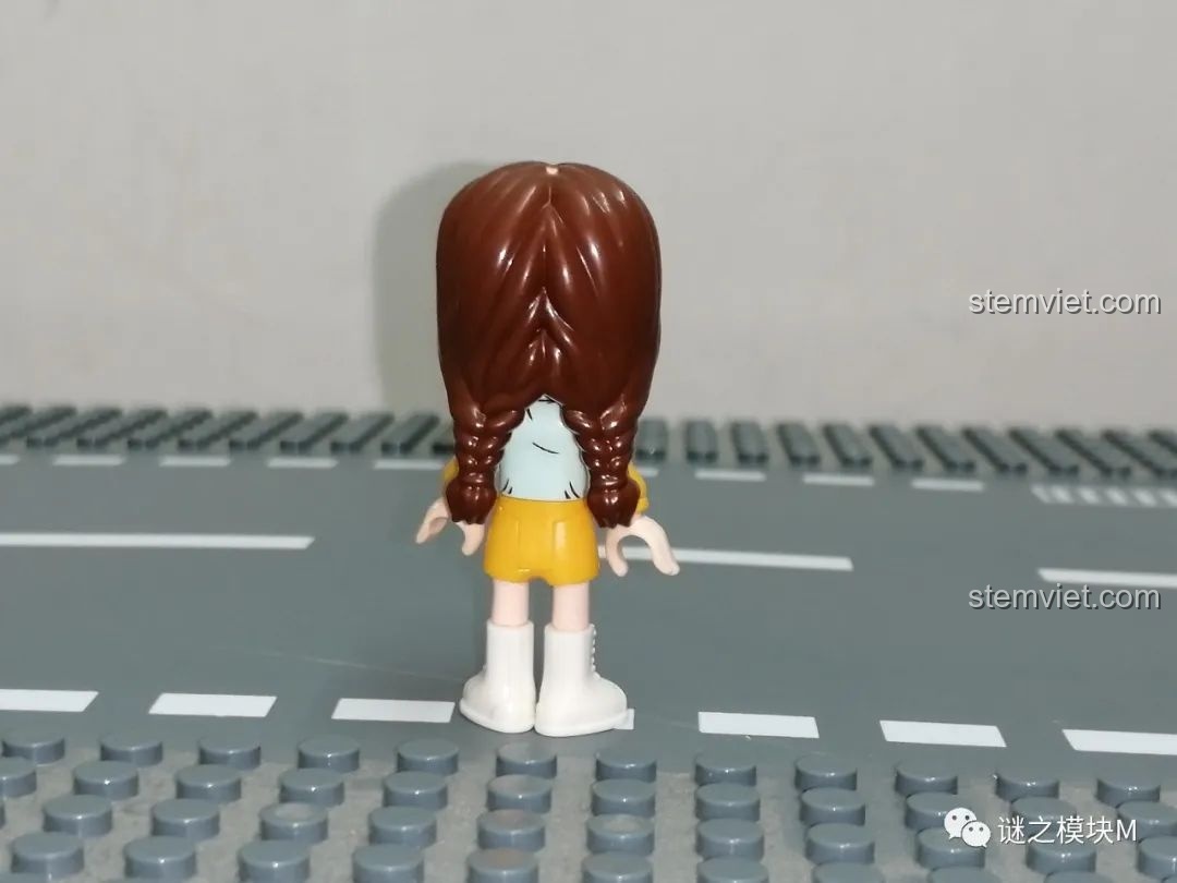 Mặt sau của minifigure Nhiếp ảnh gia UNA 34011 với mái tóc tết và áo in họa tiết.