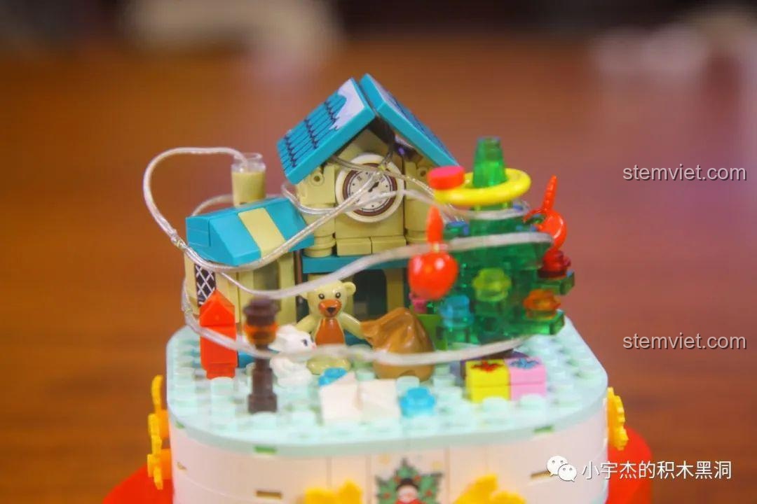 Quấn dây đèn LED quanh mô hình nhà và cây thông trong bộ Hộp Nhạc Giáng Sinh Người Tuyết.