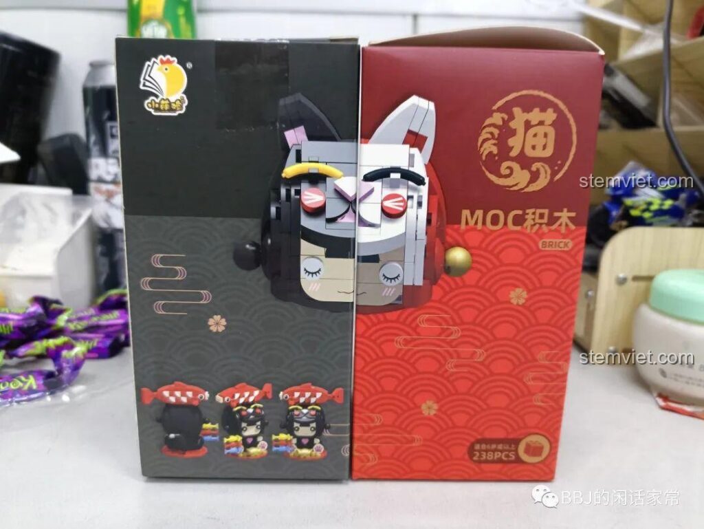 Hộp của hai bộ lắp ráp Mèo Thần Tài Xiao Meng Ji 2054 và 2053 đặt cạnh nhau, thể hiện thiết kế đối lập độc đáo.