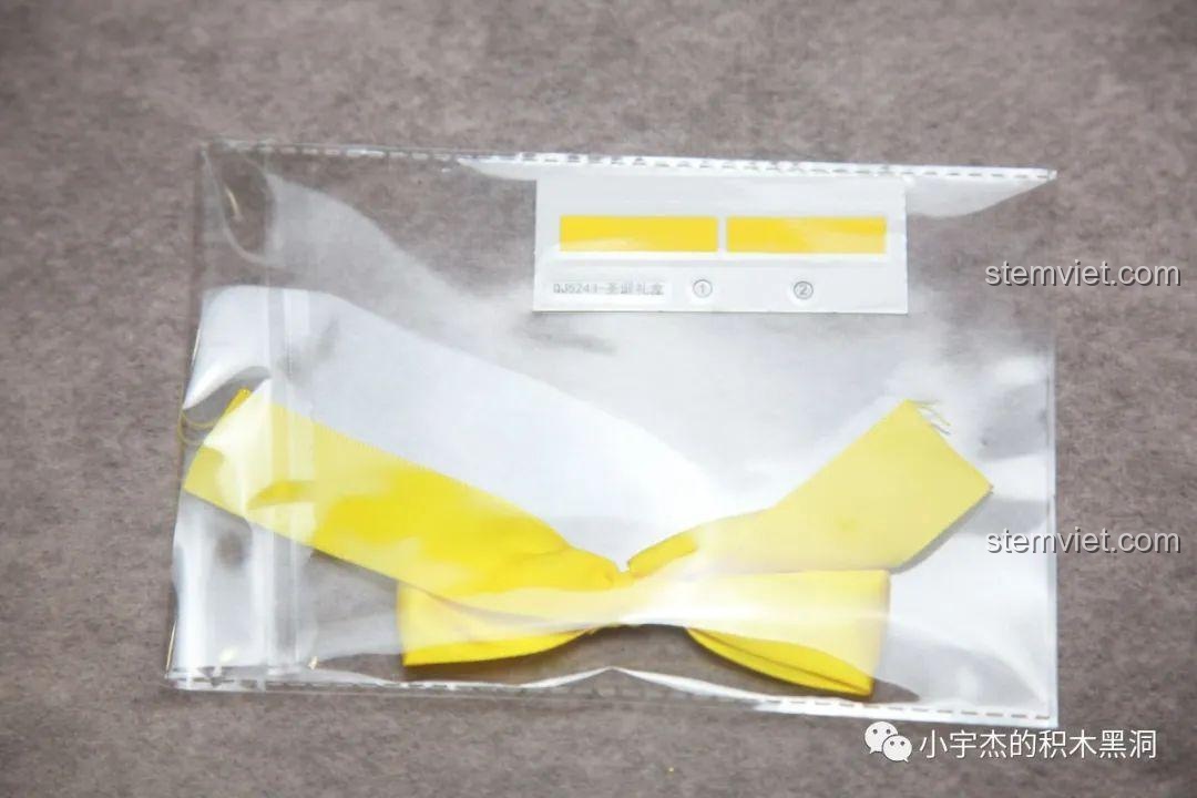 Tấm sticker và chiếc nơ vàng đi kèm bộ lắp ráp Hộp Quà Giáng Sinh QJ5243, dùng để trang trí mô hình.