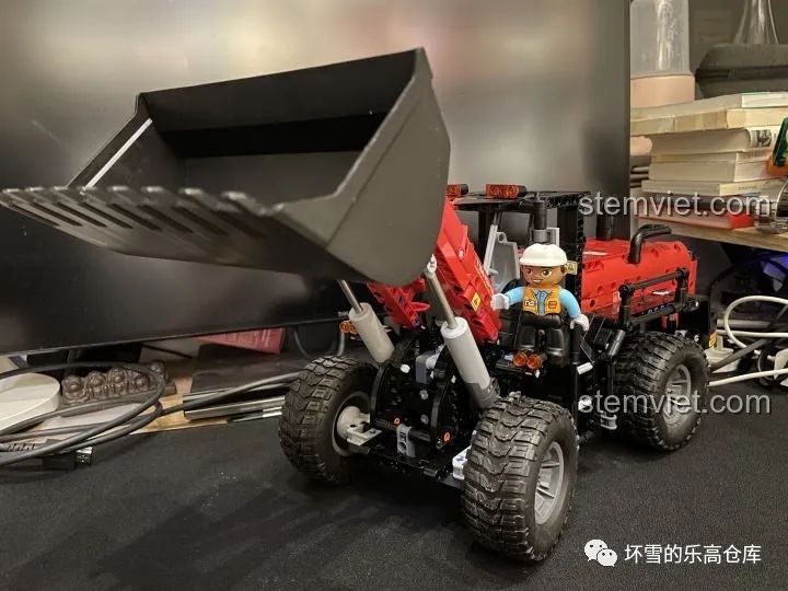 Mô hình Xe Xúc Lật Công Trình ONEBOT OBZZJ01AIQI đang trong quá trình lắp ráp, với một nhân vật minifig đứng cạnh.