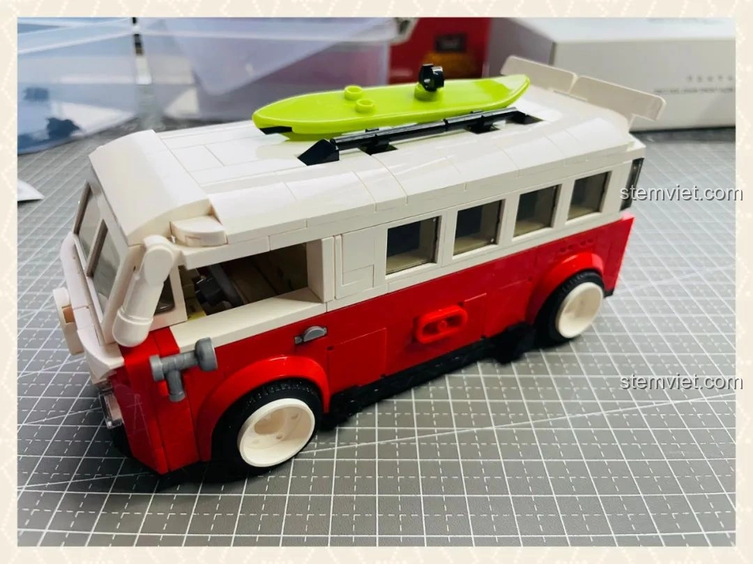 Mô hình Pinbo PB8807 Xe Cắm Trại T1 Thời Gian Hè đã hoàn thiện, với màu đỏ trắng đặc trưng và ván lướt sóng trên mái.