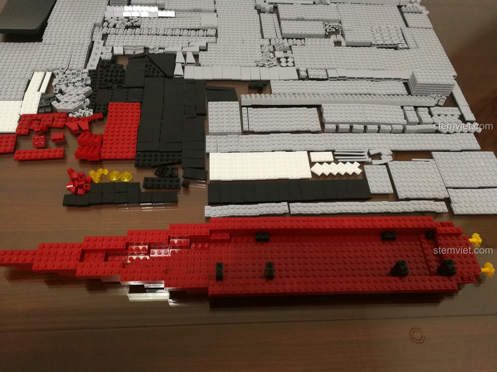 Quá trình bắt đầu lắp ráp bộ Sluban 399 Mô hình tàu sân bay Liêu Ninh, với các mảnh ghép màu đỏ và xám được sắp xếp để tạo thành phần đế và vỏ tàu.