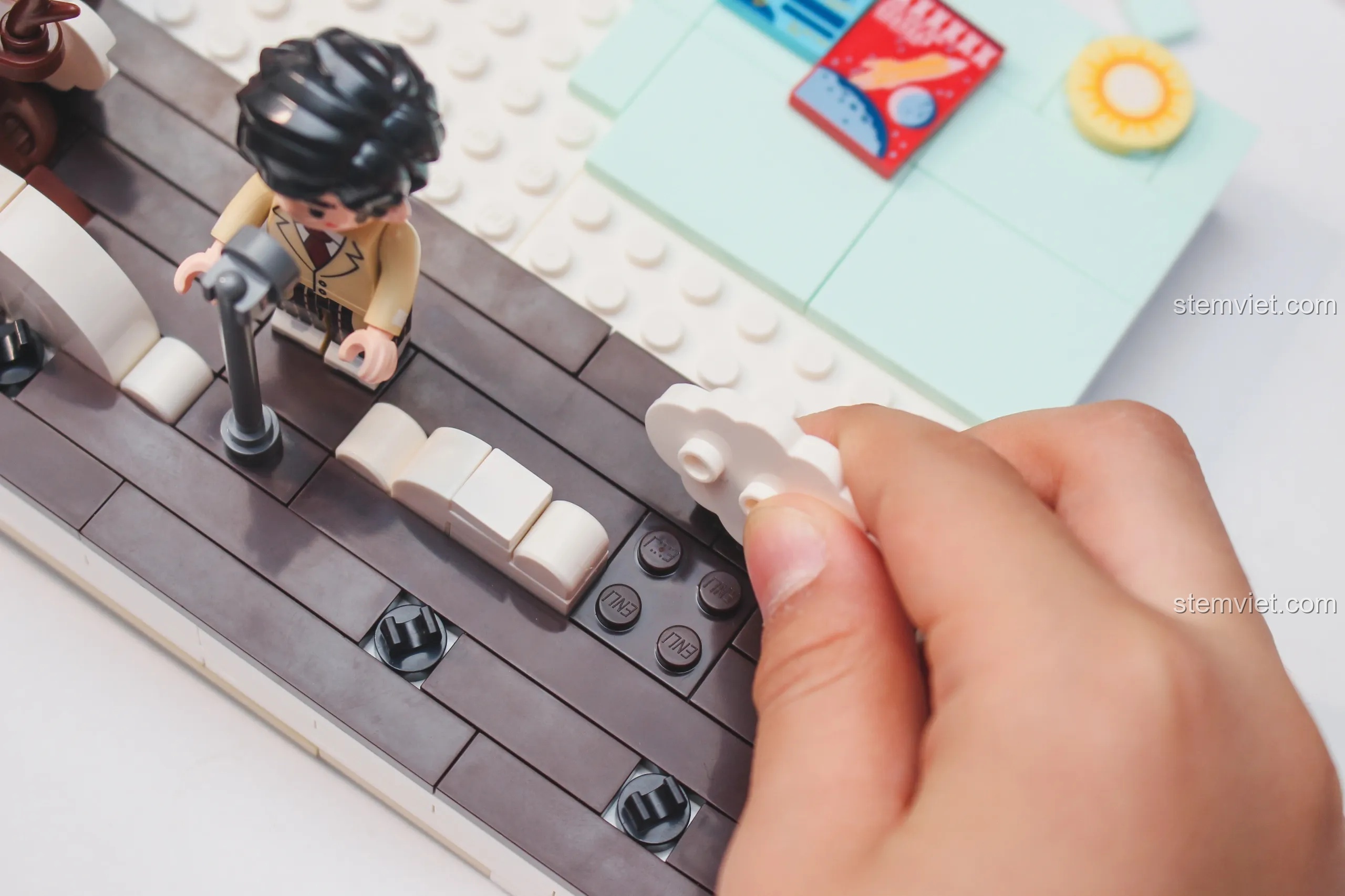 Một bàn tay đang lắp ráp các chi tiết nhỏ trên sân khấu của mô hình Keeppley Đàn Piano Châu Kiệt Luân.