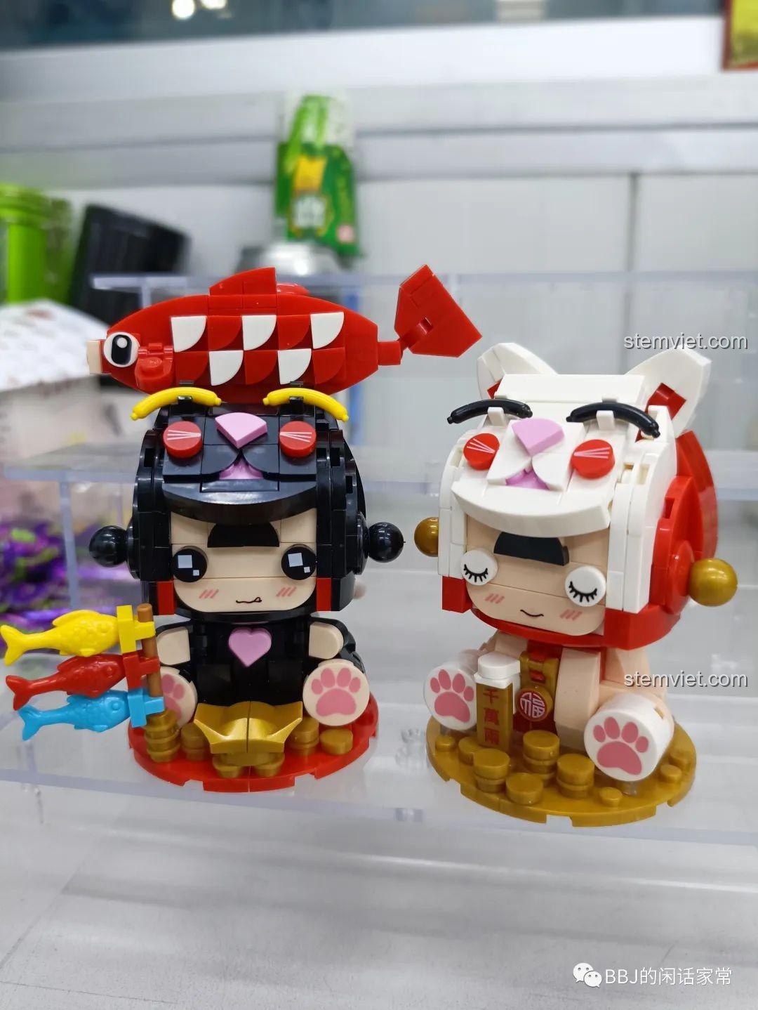 Ảnh chụp cận cảnh mô hình Mèo Thần Tài Koi 2054 và Mèo Đa Tài 2053 đứng cạnh nhau, một bộ sưu tập đáng yêu.