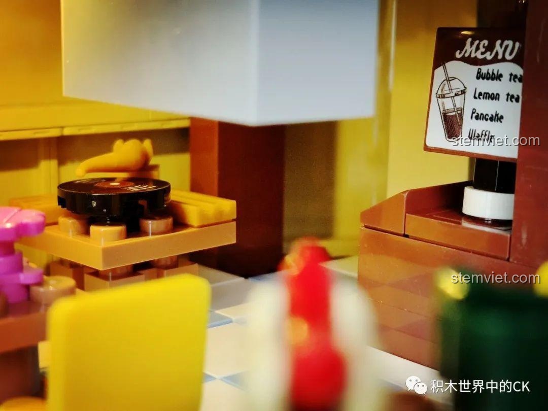 Khu vực bàn ghế tầng hai của mô hình Cửa hàng trà sữa JIAZHI SY 5209, với hotdog và cốc nước.