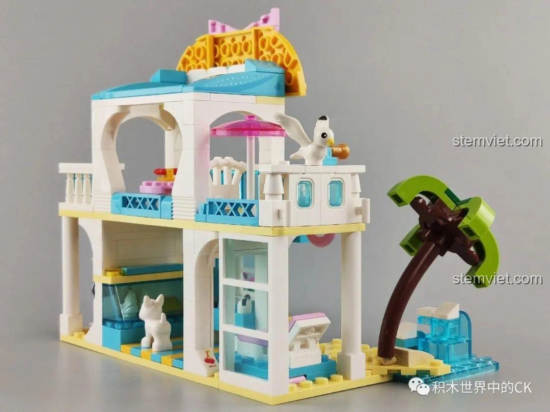 Mô hình biệt thự bãi biển QMAN 4804 hoàn thiện, nhìn từ phía sau bên trái, với cây cọ và thác nước nhỏ.