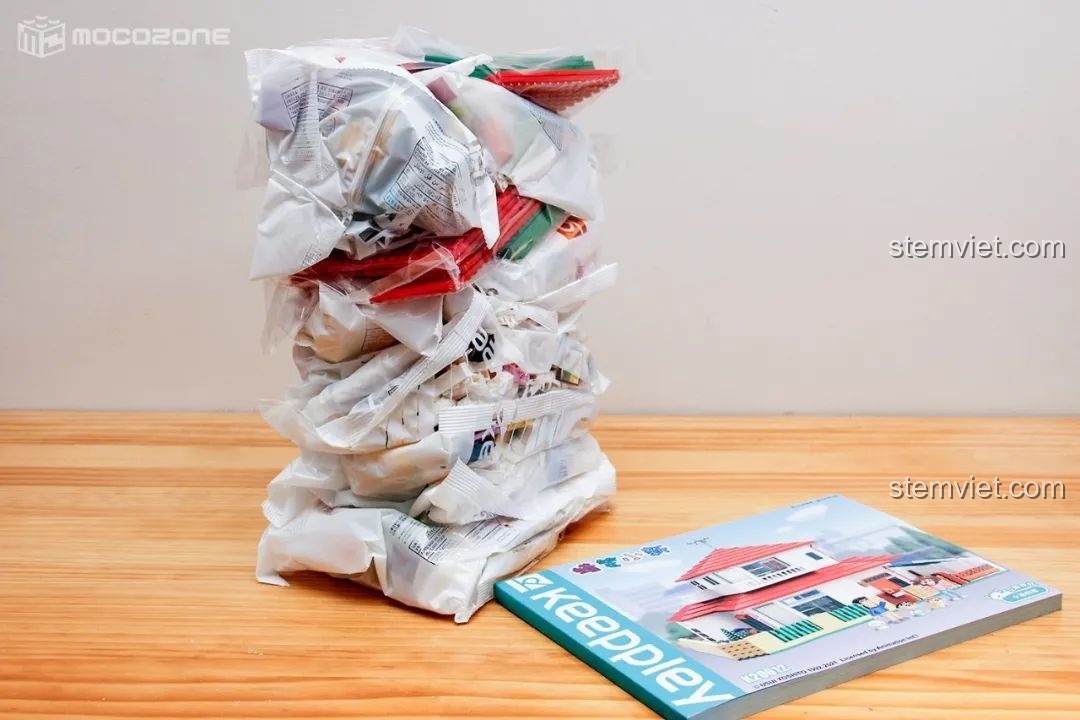 Toàn bộ các túi mảnh ghép của bộ lắp ráp Tổ ấm của gia đình Shin-chan và sách hướng dẫn dày dặn đặt trên bàn gỗ.