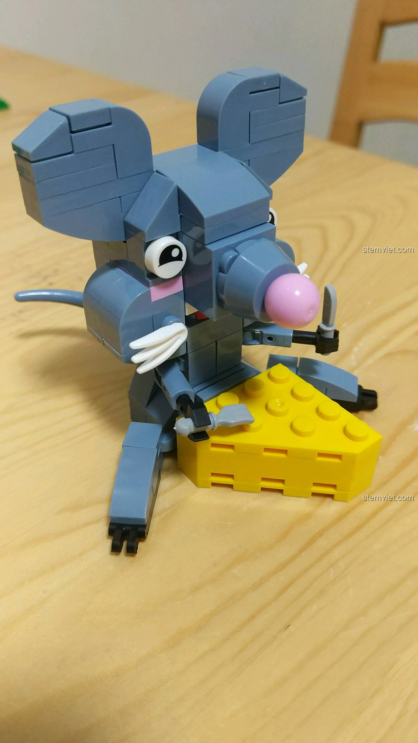 Mô hình Chuột Tý màu xám đang ôm miếng phô mai vàng, với đôi mắt to tròn và râu trắng.