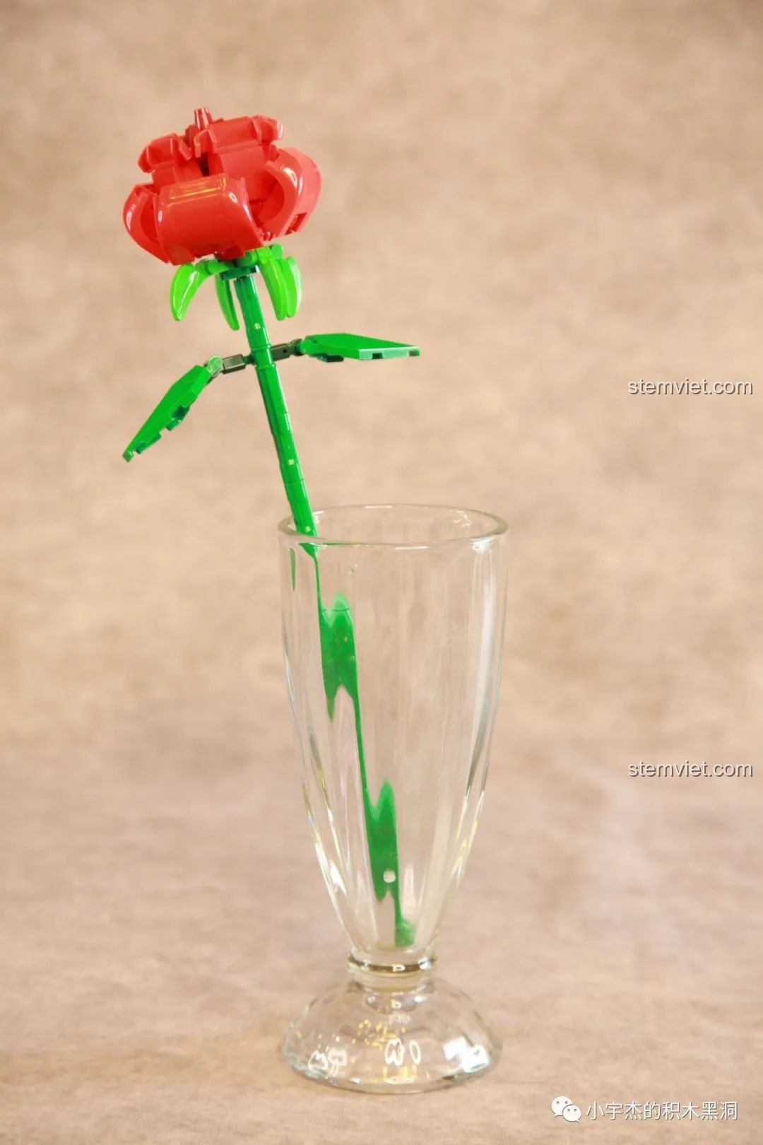 Một cành hoa hồng đỏ từ bộ lắp ráp SEMBO 601268 được cắm trong ly thủy tinh cao, đơn giản mà tinh tế.