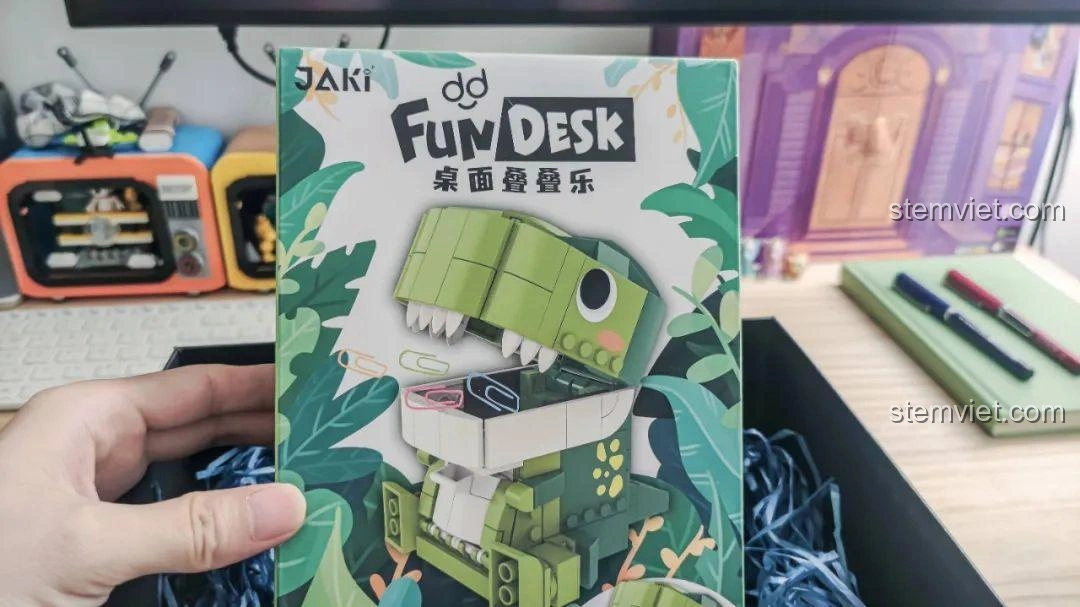 Người dùng cầm hộp đồ chơi lắp ghép Khủng long Bạo Chúa Ăn Vặt JAKI JK5102, cho thấy kích thước thực tế của sản phẩm.