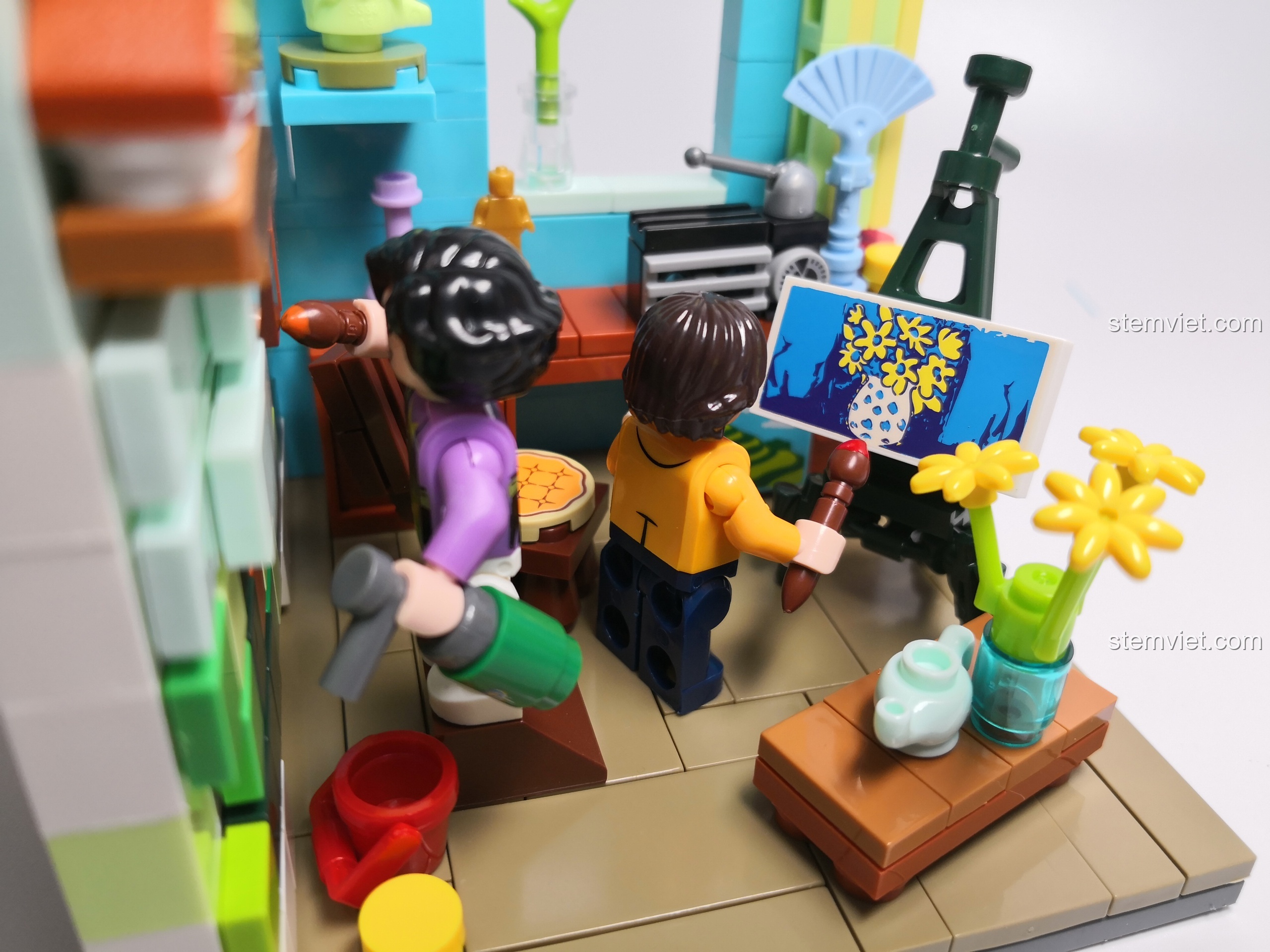 Cận cảnh hai minifigure họa sĩ đang vẽ tranh trong phòng làm việc, với các chi tiết nhỏ như giá vẽ, bình hoa được thể hiện tinh xảo.