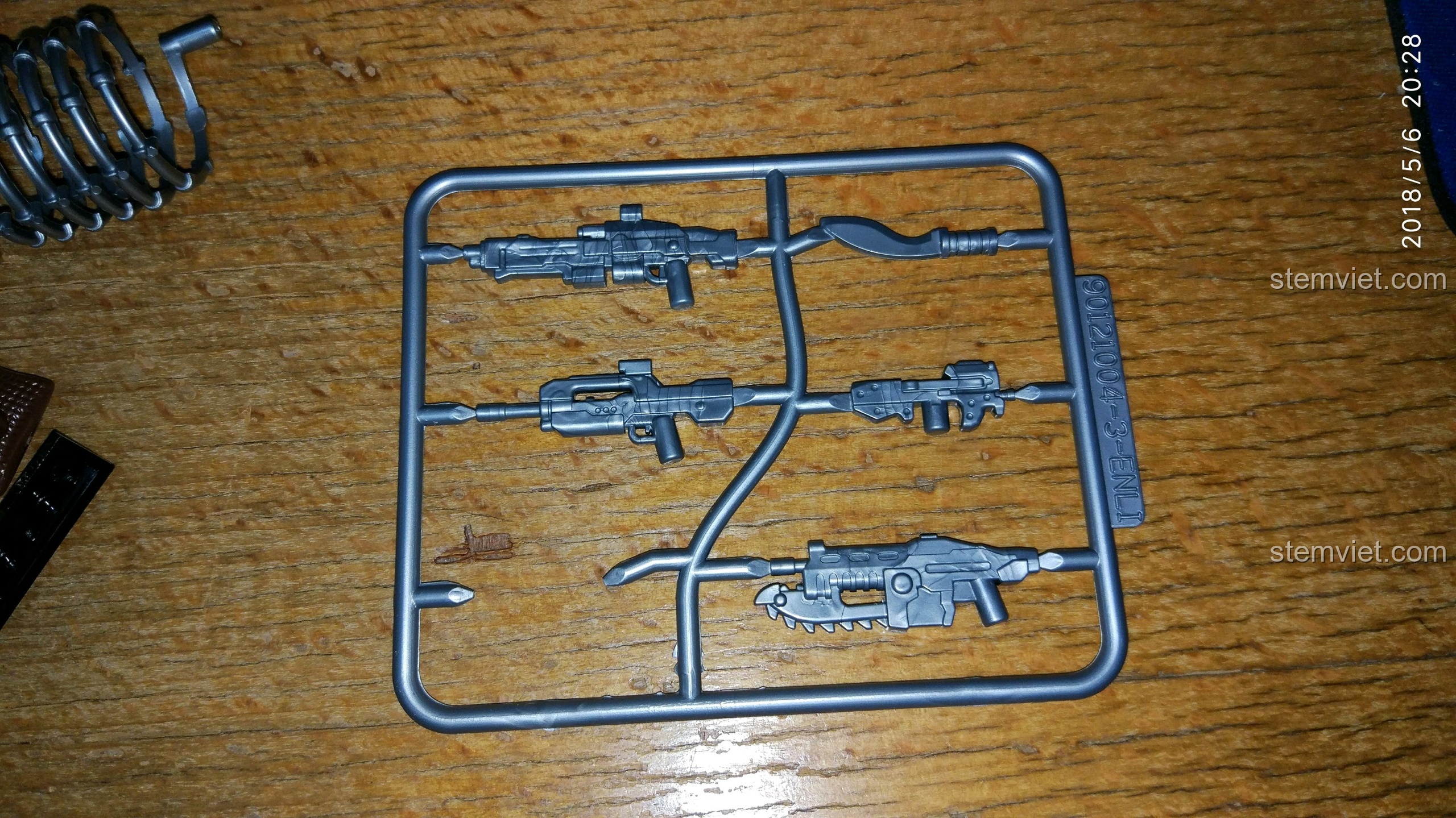 Cận cảnh một vỉ vũ khí màu bạc trong bộ đồ chơi QMAN với các chi tiết sắc nét, không có nhựa thừa.