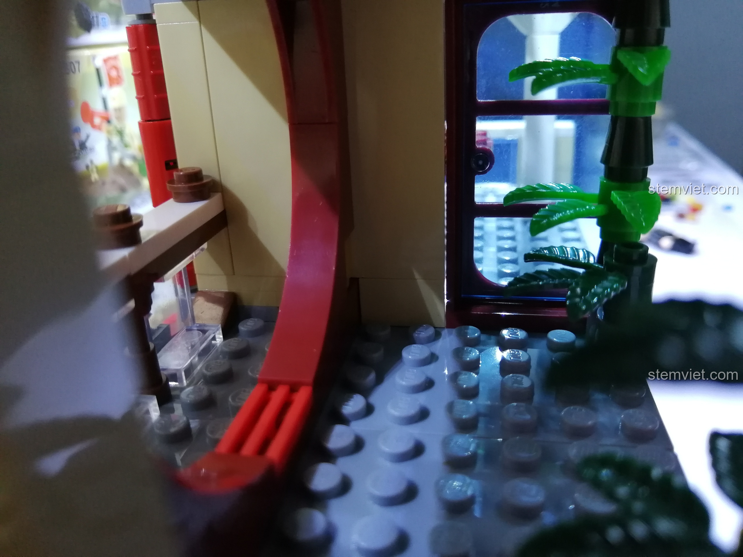 Cầu thang màu đỏ dẫn lên tầng hai và chậu cây tre trang trí trong mô hình nhà hàng QMAN 1137.