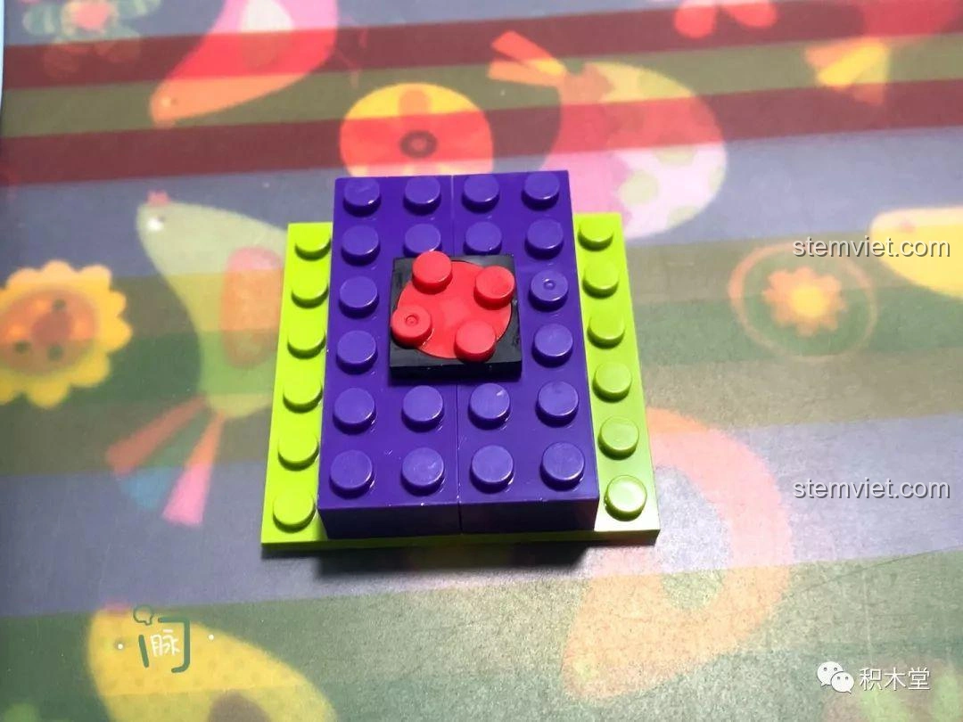 Mảnh ghép nền màu xanh lá và tím với một chi tiết tròn màu đỏ ở trung tâm, dùng làm đế cho cỗ máy bạch tuộc của Buzz Lightyear.