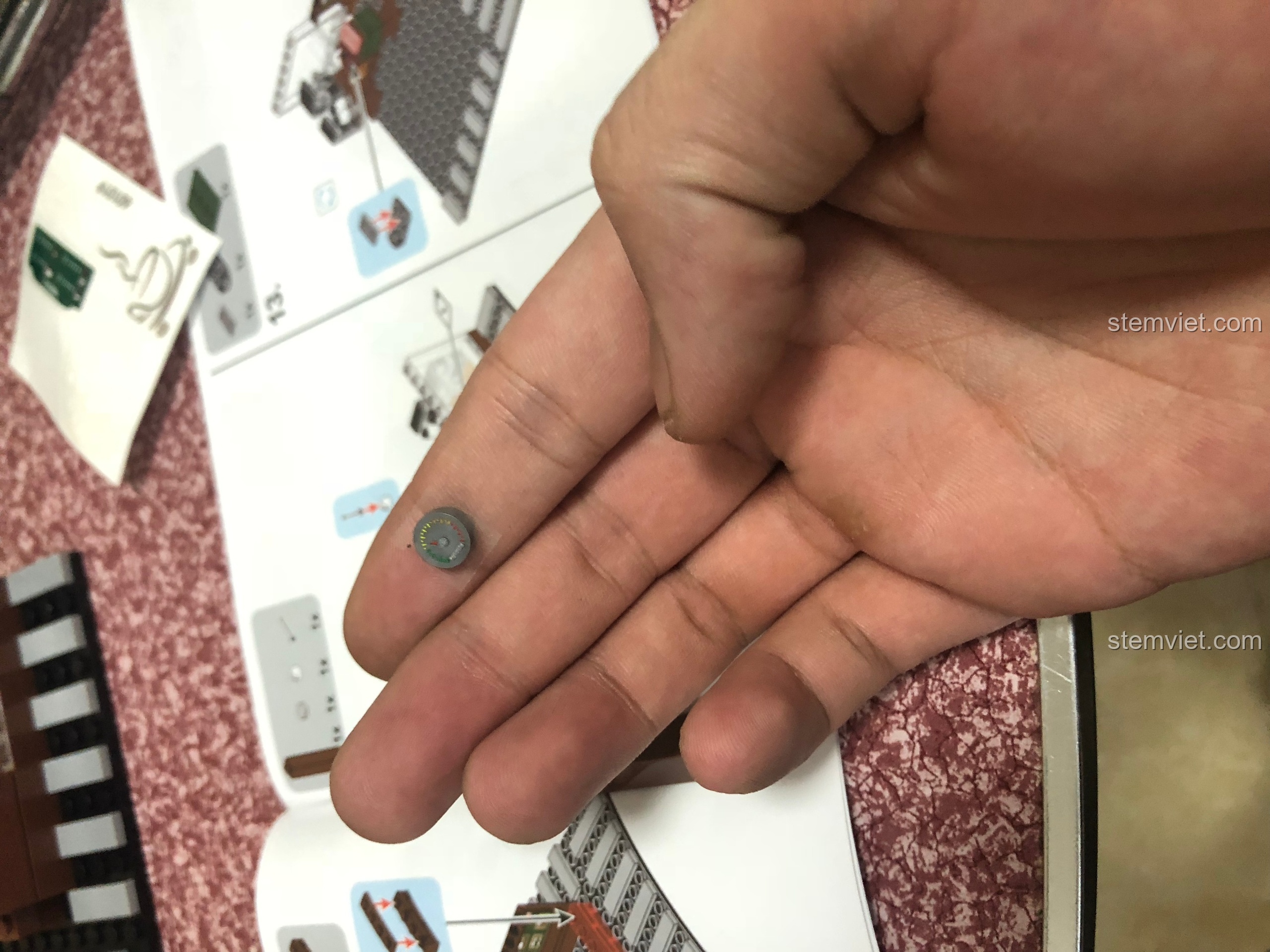 Một mảnh ghép tròn nhỏ với sticker bị dán lỗi, hình ảnh không hoàn hảo, nằm trên lòng bàn tay.