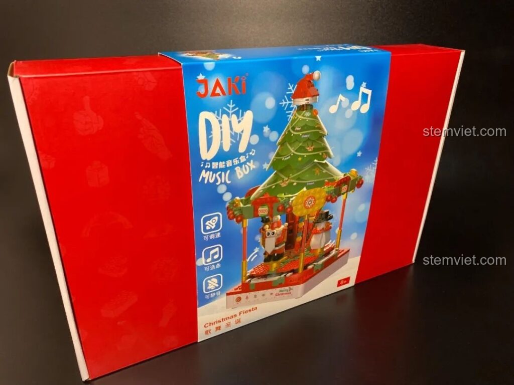 Hộp nhạc Giáng Sinh Xoay Tự Động JAKI JK1365 với bao bì đỏ rực rỡ, hình ảnh cây thông và các nhân vật Giáng Sinh đáng yêu. Đồ chơi lắp ráp Giáng Sinh có nhạc.