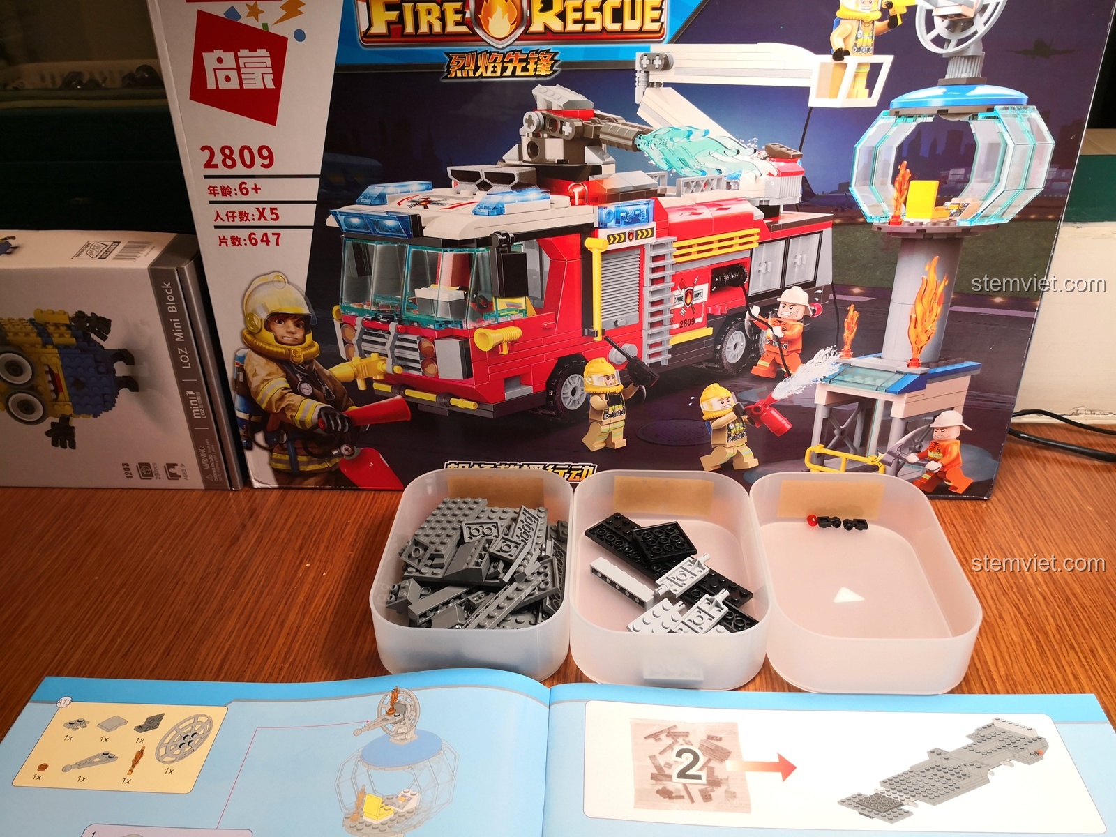 Chuẩn bị lắp ráp bộ đồ chơi cứu hỏa thành phố QMAN 2809 với sách hướng dẫn và các chi tiết được đổ ra khay.