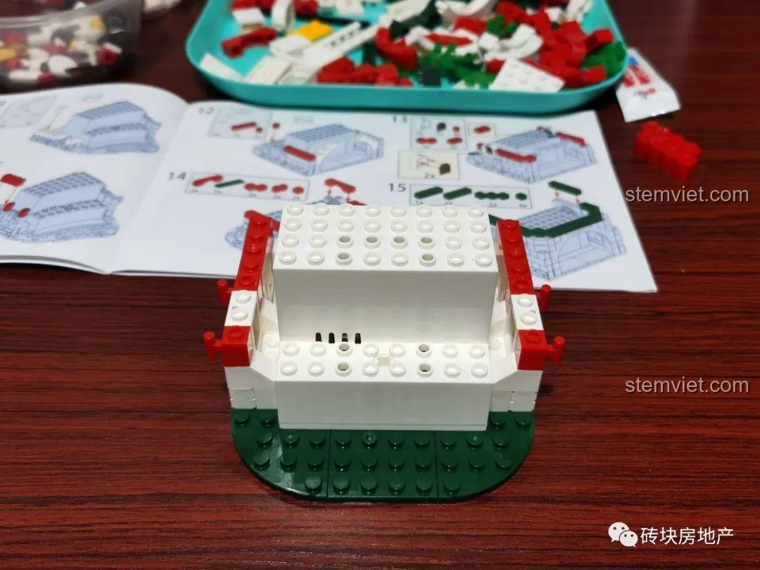 Cấu trúc phần đế của mô hình Hộp nhạc Giáng Sinh Zhe Gao QL0981 đang được xây dựng, với các mảnh ghép màu đỏ và trắng.