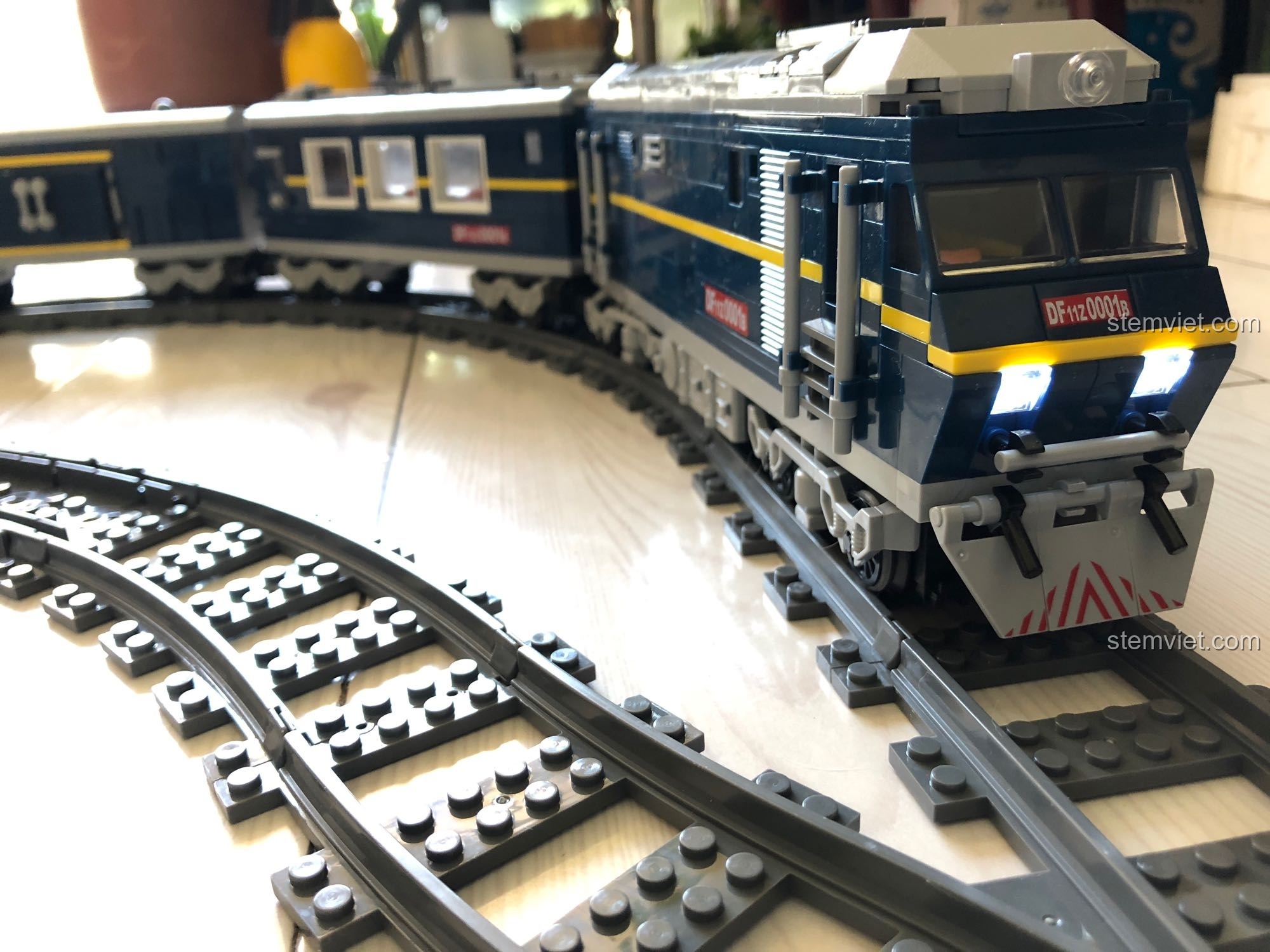 Cận cảnh mô hình KAZI 98220 Tàu Hỏa Đông Phong 11Z đang chạy trên đường ray, đèn pha sáng rõ.