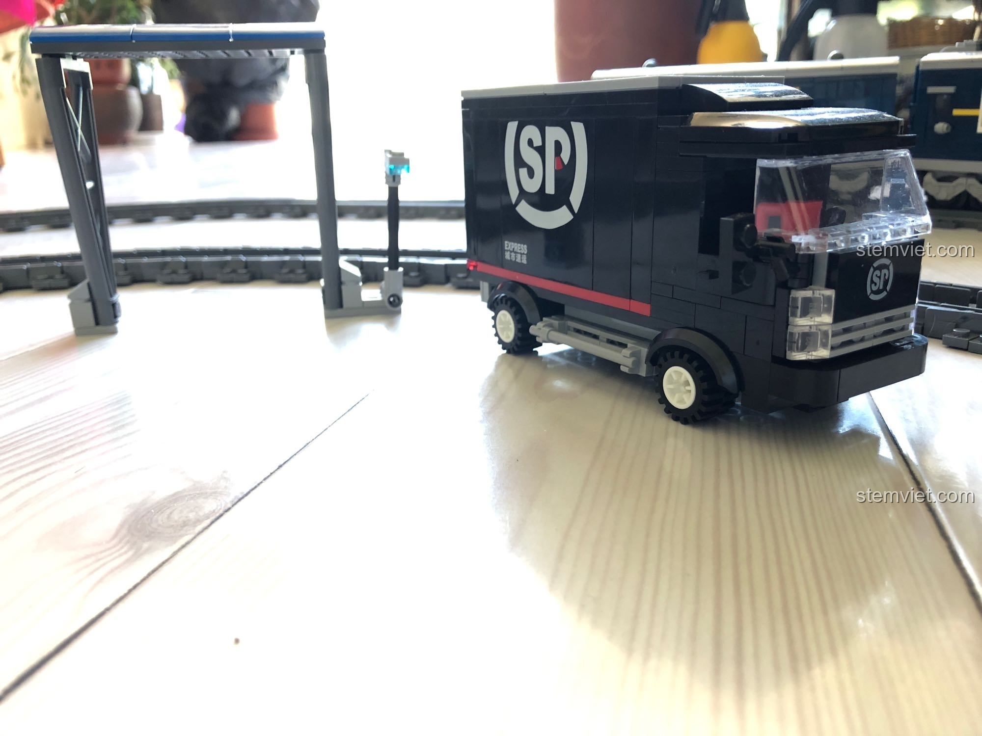 Mô hình xe tải vận chuyển SP City Express đặt cạnh đường ray của bộ KAZI 98220 Tàu Hỏa Đông Phong 11Z, tạo bối cảnh.