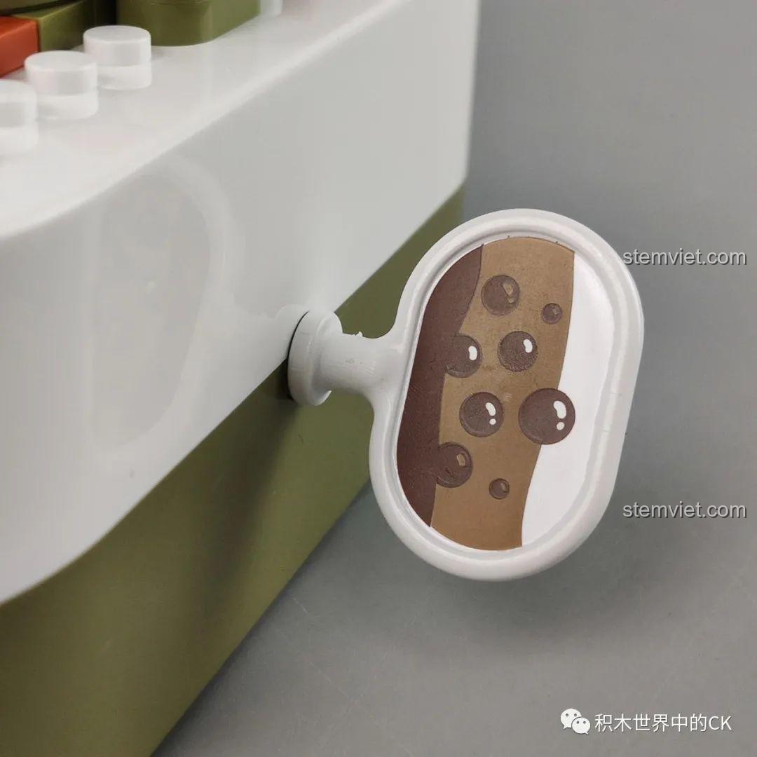 Cận cảnh cần gạt của hộp nhạc trà sữa JAKI, được thiết kế hình giọt nước hoặc bọt sữa độc đáo.