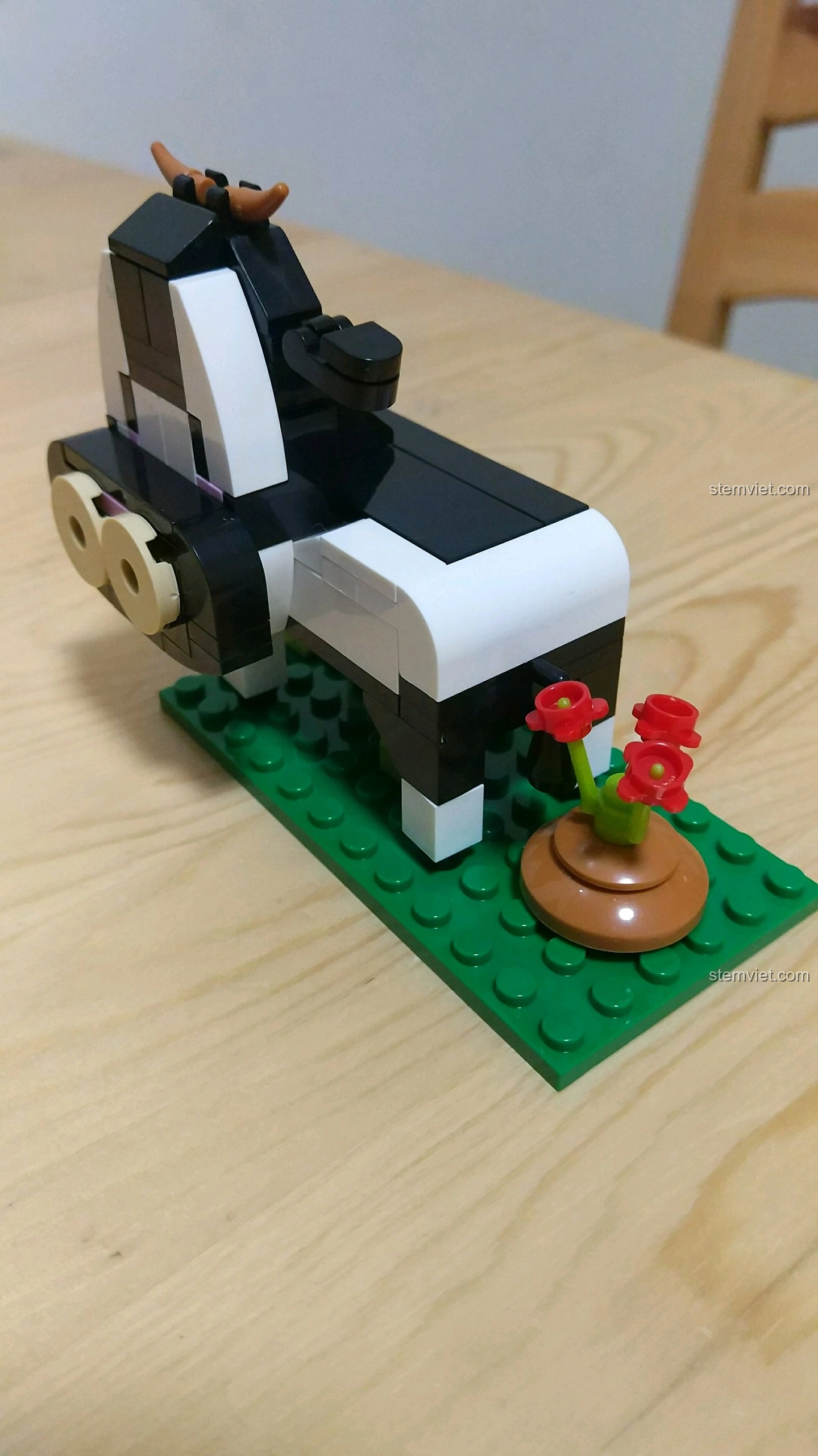 Góc nghiêng của mô hình Trâu Sửu, cho thấy chi tiết thân hình đen trắng và đống phân bò có hoa bên cạnh.