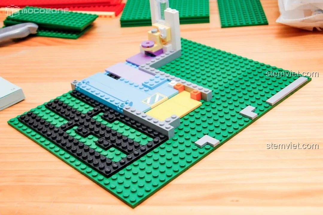 Quá trình lắp ráp tầng một của mô hình nhà của Cậu bé bút chì, bắt đầu với phần móng và sàn nhà trên tấm nền xanh.