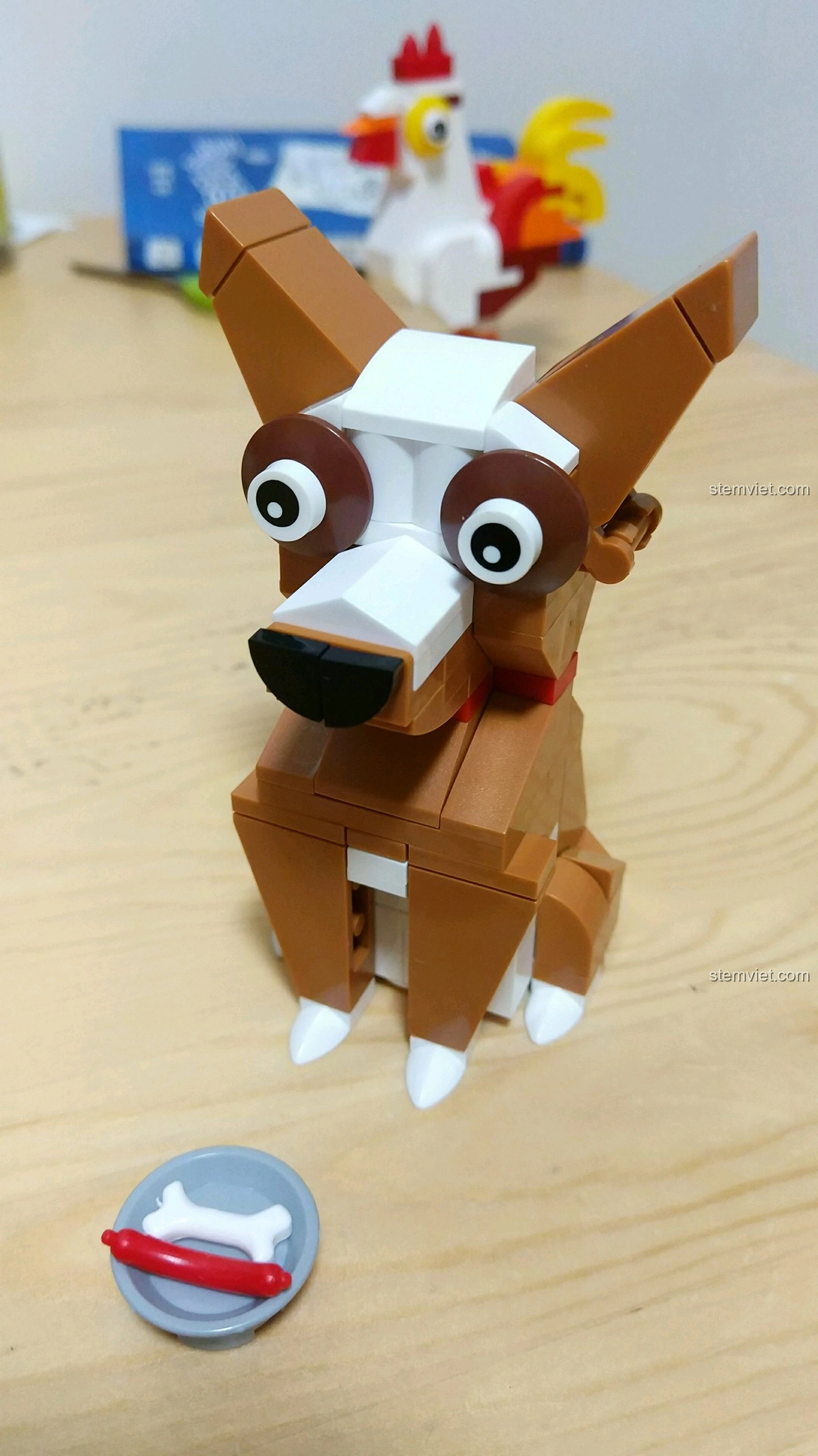 Mô hình Chó Tuất màu nâu trắng, ngồi cạnh bát thức ăn có xương và xúc xích, tạo hình giống chó Chihuahua.