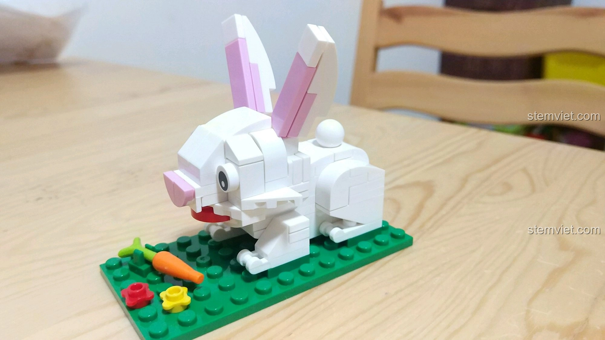 Góc nghiêng của mô hình Thỏ Mão, cho thấy chi tiết tai hồng và thân trắng, ngồi trên nền cỏ xanh.