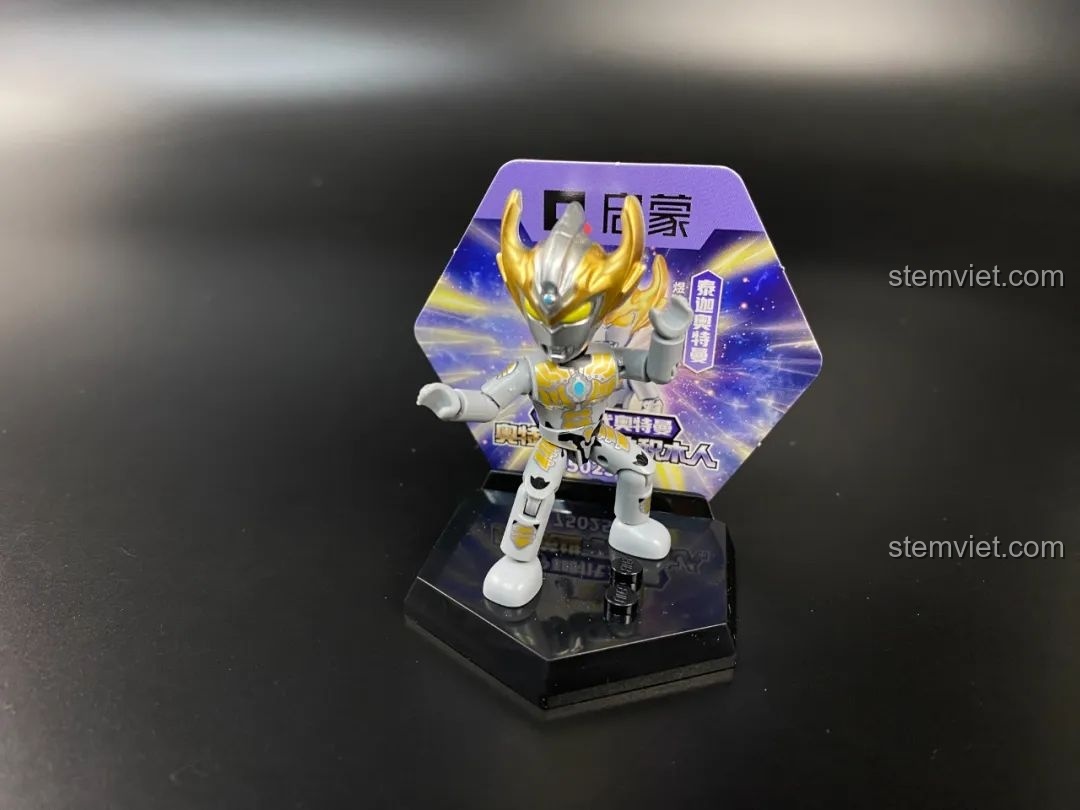 Figure Ultraman Taiga Tri-Strium được trưng bày trên đế cùng với thẻ bài nhân vật.