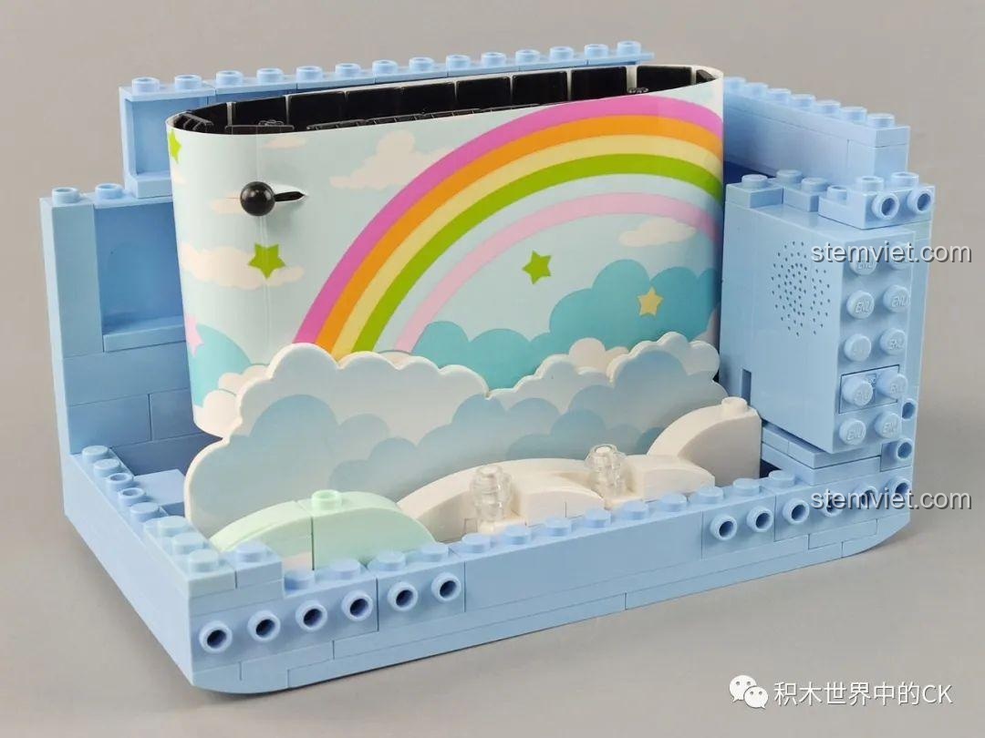 Gắn tấm nền cầu vồng và khối phát nhạc vào khung của bộ lắp ráp Tivi Doraemon Keeppley 20408, tạo nên khung cảnh chính.