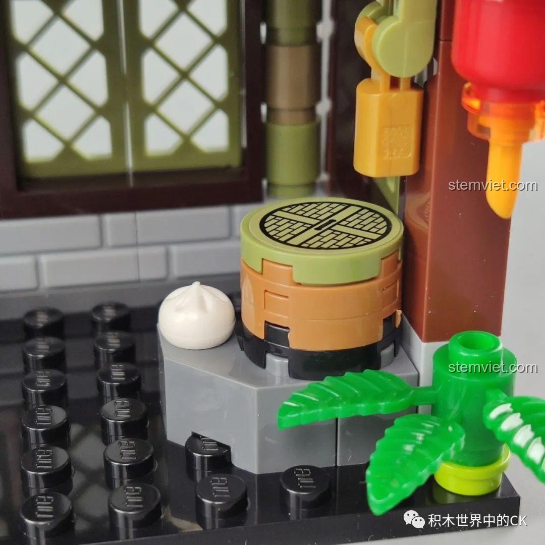 Góc quầy hàng bên trong mô hình Tiệm Bánh Bao Vô Song QMAN 72012, với nồi hấp và cây xanh.