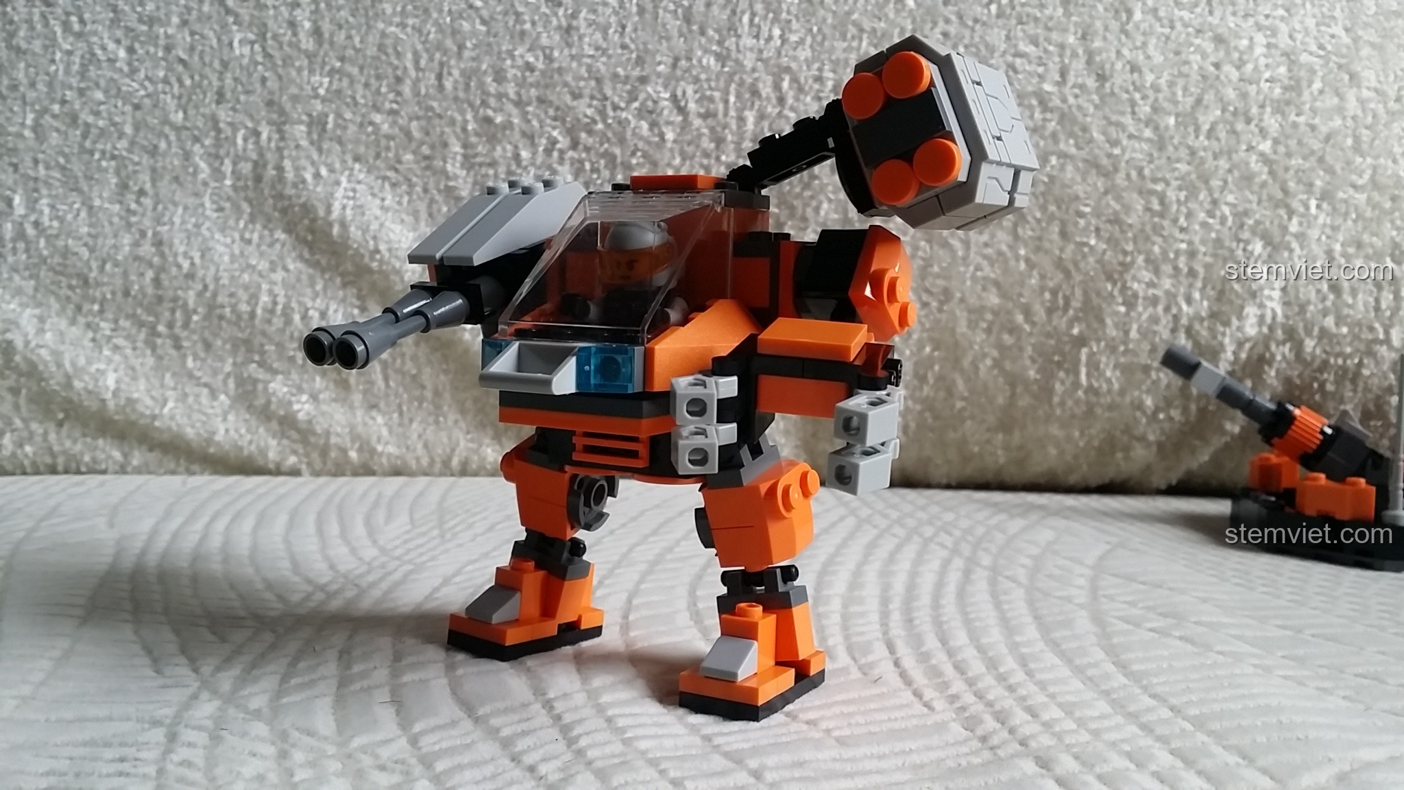 Robot GUDI 8224 SkyNet Bombard đứng cạnh khẩu pháo nhỏ đi kèm, sẵn sàng chiến đấu.