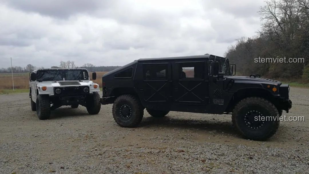 Hai chiếc xe địa hình Humvee H1 màu trắng và đen đang đỗ trên đường đất, thể hiện sự đa dạng của dòng xe này.