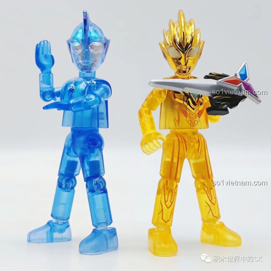 Hai mô hình Ultraman, một là Ultraman Fusion Rise trong suốt màu xanh và một là Ultraman Gauss màu vàng, cả hai đều từ bộ lắp ráp BLOKEES.