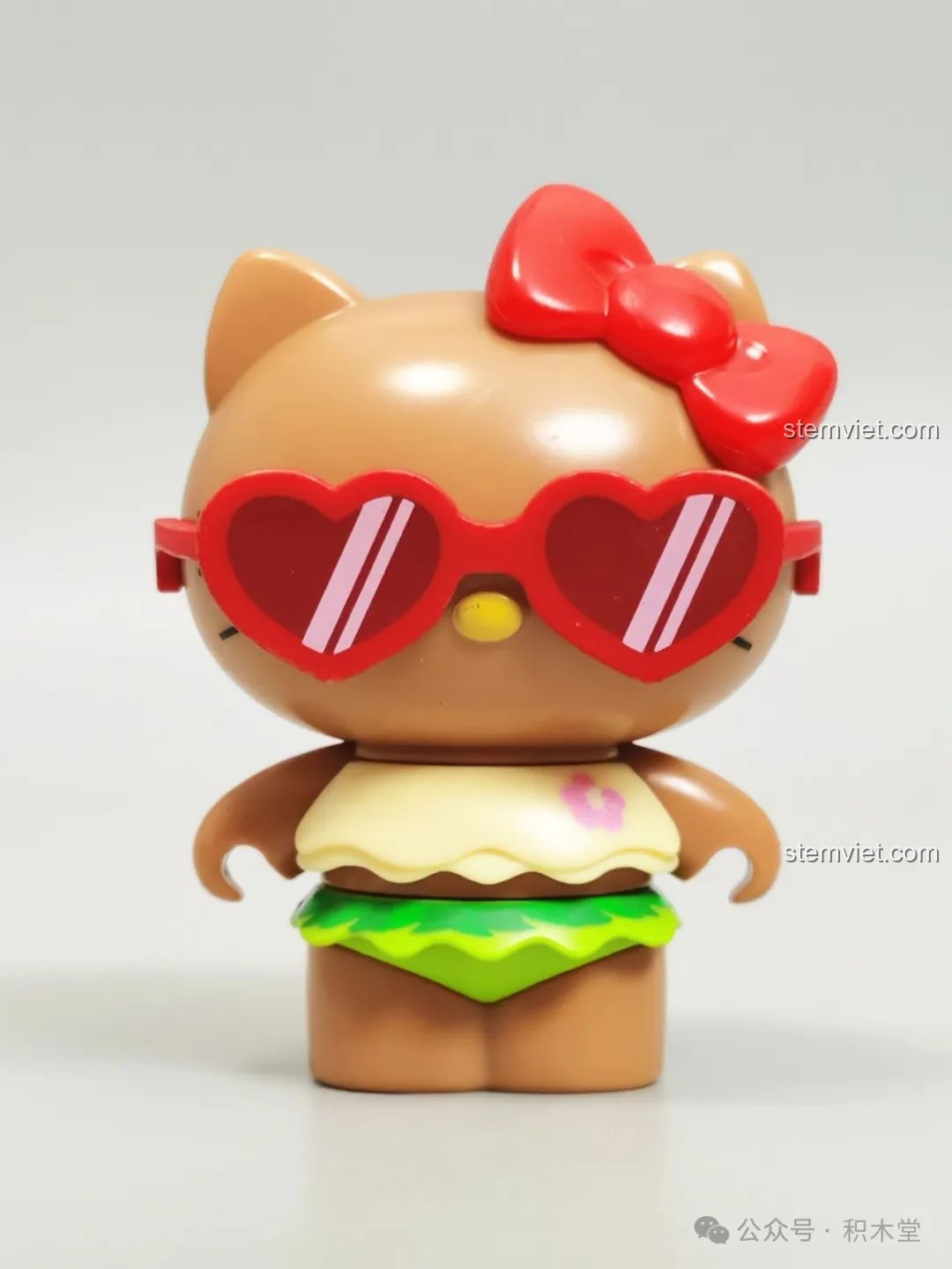 Mô hình Hello Kitty da nâu trong bộ trang phục Hawaii và kính râm đỏ, một phần của bộ đồ chơi lắp ráp Lễ Hội Âm Nhạc TOP TOY.